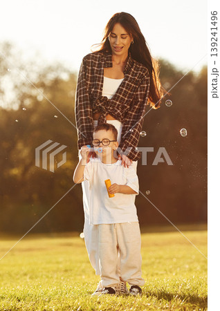 Front view, blowing bubbles. Mother and son together in an open field during daytime 139241496