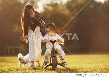 Learning to ride a bicycle. Mother and son together in an open field during daytime Learning to ride a bicycle. Mother and son together in an open field during daytime 139241502