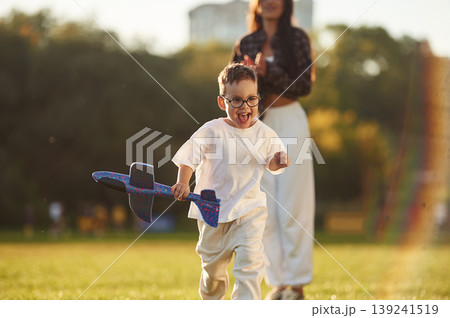 Blue colored toy plane is in hand. Mother and son together in an open field during daytime Blue colored toy plane is in hand. Mother and son together in an open field during daytime 139241519
