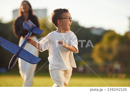 Blue colored toy plane is in hand. Mother and son together in an open field during daytime Blue colored toy plane is in hand. Mother and son together in an open field during daytime 139241520