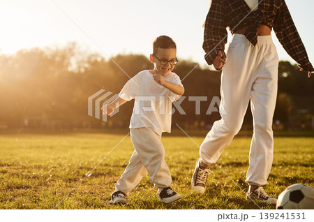 Running, playing soccer. Mother and son together in an open field during daytime Running, playing soccer. Mother and son together in an open field during daytime 139241531