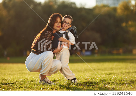 Back to school conception, with backpack. Mother and son together in an open field during daytime Back to school conception, with backpack. Mother and son together in an open field during daytime 139241546
