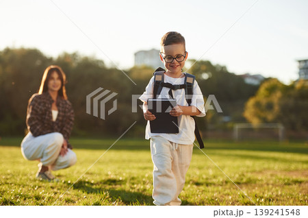 Pupil is with book and backpack. Mother and son together in an open field during daytime 139241548