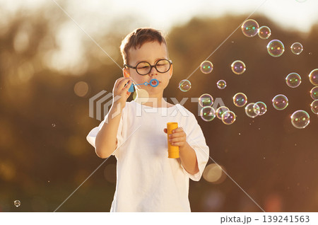 Blowing bubbles. Boy is having fun on the field under sunlight at daytime Blowing bubbles. Boy is having fun on the field under sunlight at daytime 139241563