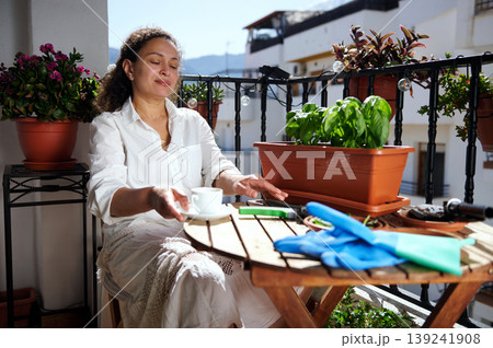 Woman Relaxing on Sunny Balcony With Potted Herbs, Coffee and Gardening Gloves 139241908