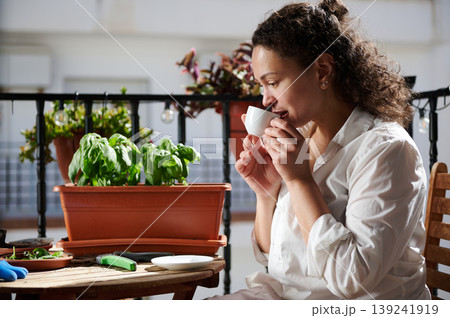 Woman Drinking Coffee on Balcony While Tending Potted Basil Plants in Morning Urban Garden Woman Drinking Coffee on Balcony While Tending Potted Basil Plants in Morning Urban Garden 139241919