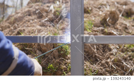 Worker Securing Steel Post With Wire, Closeup Of Gloved Hand At Private House Construction Site, Metal Frame Upright In Muddy Yard, Focus On Manual Tying Technique, Calm Practical 139243140