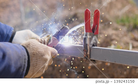 Worker Welding Clamped Joint Producing Bright Sparks And Molten Bead Closeup Shows Clamp Handles And Torch Angle Securing Two Steel Pieces For Permanent Fusion, Smoke And Light Highlight Worker Welding Clamped Joint Producing Bright Sparks And Molten Bead Closeup Shows Clamp Handles And Torch Angle Securing Two Steel Pieces For Permanent Fusion, Smoke And Light Highlight 139243150