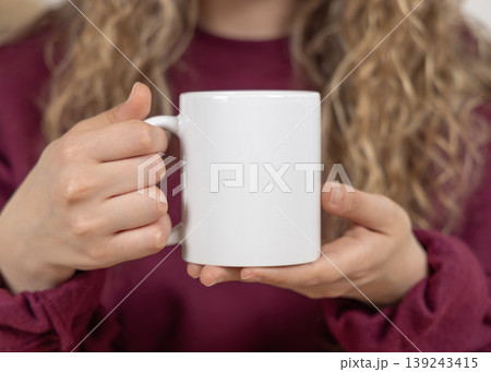 Blank white 11 oz mug mockup in hand of fair-haired woman closeup, ceramic cup template 139243415