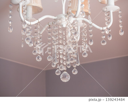 White chandelier with hanging crystal glass pendants. Elegant interior ceiling lighting for home decor. Decorative lamp with gem-like refraction for luxury room design and living space. White chandelier with hanging crystal glass pendants. Elegant interior ceiling lighting for home decor. Decorative lamp with gem-like refraction for luxury room design and living space. 139243484