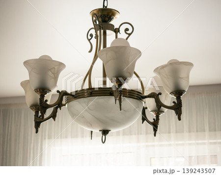 Antique brass chandelier with frosted glass shades hanging from ceiling. Elegant vintage light fixture for interior home decoration. Luxurious lighting design for classic room style. Antique brass chandelier with frosted glass shades hanging from ceiling. Elegant vintage light fixture for interior home decoration. Luxurious lighting design for classic room style. 139243507