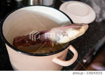 Raw beef tongue in metal pot. Process of preparing traditional meat dish. Organ food ingredient for cooking at home kitchen. Uncooked protein product for culinary meal preparation. Raw beef tongue in metal pot. Process of preparing traditional meat dish. Organ food ingredient for cooking at home kitchen. Uncooked protein product for culinary meal preparation. 139243535
