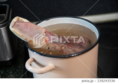 Boiled beef tongue in pot on stove. Raw meat cooking in water. Preparation of traditional appetizer or gourmet dish. Culinary process in kitchen for homemade meal or restaurant menu. 139243536
