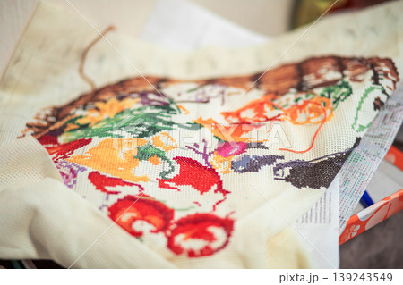 Embroiderer working on a cross stitch pattern on canvas. Colorful handmade needlework project with embroidery floss. Concept of hobby, craft, art, leisure activity and creative workshop. 139243549