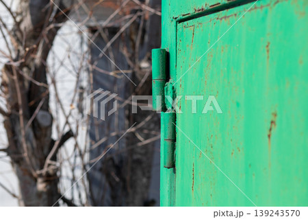 Green metal door hinge on an old rusted gate. Close up of an industrial hardware mechanism. Texture of weathered iron construction element with paint decay and corrosion on a rural background. Green metal door hinge on an old rusted gate. Close up of an industrial hardware mechanism. Texture of weathered iron construction element with paint decay and corrosion on a rural background. 139243570