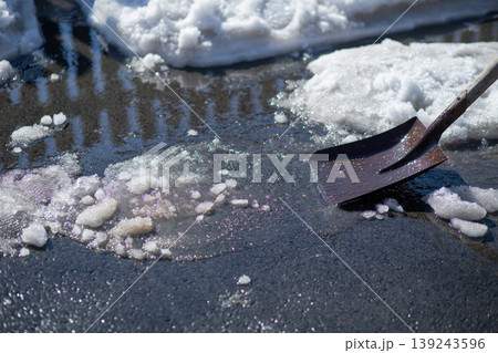 Metal shovel clearing slush and snow from sidewalk. Manual labor task during winter season. Maintenance work in cold weather conditions and icy environment for safety and winter cleanup. Metal shovel clearing slush and snow from sidewalk. Manual labor task during winter season. Maintenance work in cold weather conditions and icy environment for safety and winter cleanup. 139243596