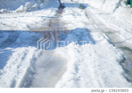 Melting snow on a rural road with deep ruts and puddles. Spring thaw transformation of winter landscape. Seasonal change and road conditions during the transition between seasons. Melting snow on a rural road with deep ruts and puddles. Spring thaw transformation of winter landscape. Seasonal change and road conditions during the transition between seasons. 139243603