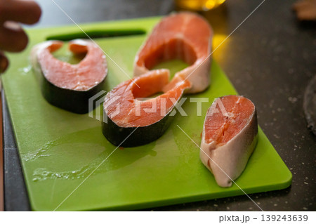 Raw salmon steak seasoned with pepper on green cutting board. Preparation of fish for cooking dinner. Healthy seafood diet and culinary concept for kitchen and home food ingredient. Raw salmon steak seasoned with pepper on green cutting board. Preparation of fish for cooking dinner. Healthy seafood diet and culinary concept for kitchen and home food ingredient. 139243639