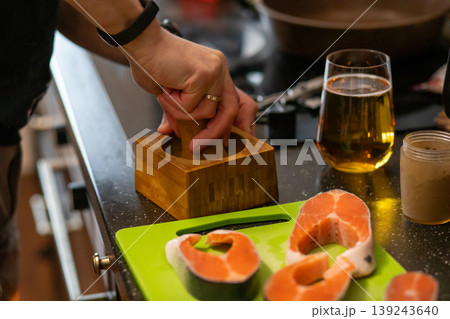Woman hand using wooden mortar and pestle in kitchen. Raw salmon steak on cutting board. Preparations for healthy dinner cooking. Culinary process at home, gastronomy, food concept. Woman hand using wooden mortar and pestle in kitchen. Raw salmon steak on cutting board. Preparations for healthy dinner cooking. Culinary process at home, gastronomy, food concept. 139243640