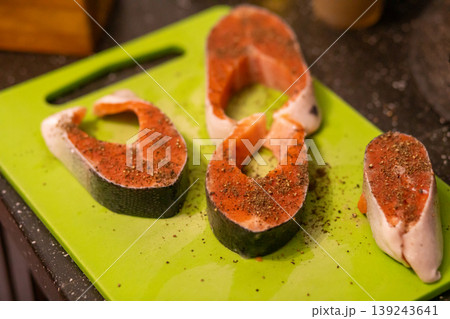 Raw salmon steak seasoned with pepper on green cutting board. Preparation of fish for cooking dinner. Healthy seafood diet and culinary concept for kitchen and home food ingredient. Raw salmon steak seasoned with pepper on green cutting board. Preparation of fish for cooking dinner. Healthy seafood diet and culinary concept for kitchen and home food ingredient. 139243641