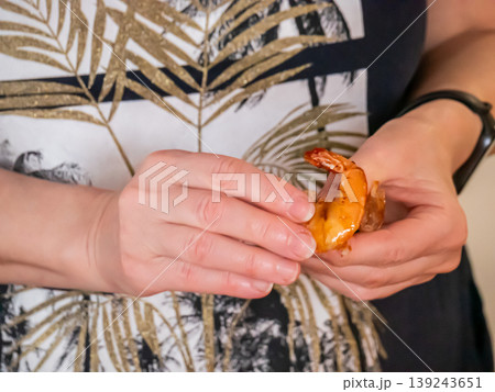 Woman peeling cooked shrimp. Culinary preparation of seafood snack. Hands cleaning crustacean before eating meal. Gastronomy, healthy protein food and kitchen activity concept in home setup. 139243651