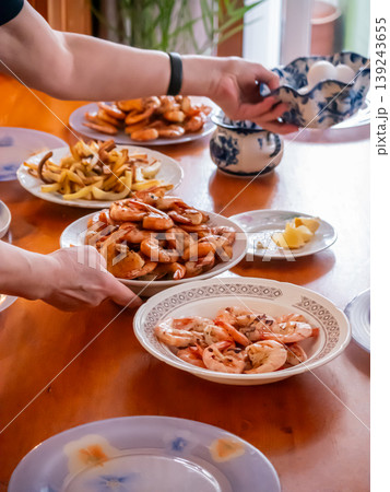 Woman serving shrimp on table. Family dinner with seafood and appetizer plates. Preparing dining meal for celebration. Home cooking and gathering, eating together, domestic lifestyle event. Woman serving shrimp on table. Family dinner with seafood and appetizer plates. Preparing dining meal for celebration. Home cooking and gathering, eating together, domestic lifestyle event. 139243655