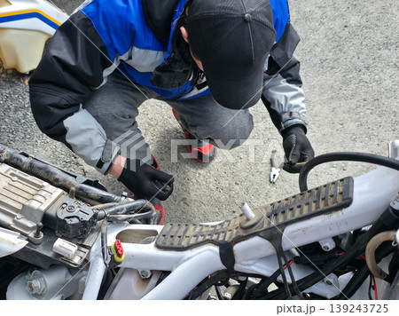 Mechanic repairing motorcycle engine. Man fixing bike frame with tool. Workshop maintenance of vehicle. Technical service, engineering and hobby concept. Troubleshooting and transport repair. 139243725