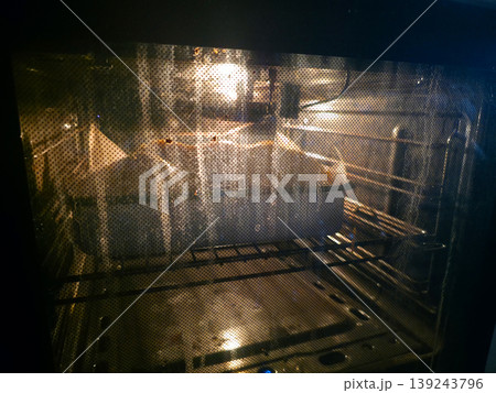 Empty oven with light turned on inside. Interior view through glass door of stainless steel kitchen appliance. Concept of cooking, baking preparation and household chore in kitchen. Empty oven with light turned on inside. Interior view through glass door of stainless steel kitchen appliance. Concept of cooking, baking preparation and household chore in kitchen. 139243796