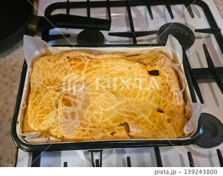 Homemade meat pie in baking tray on stove. Golden crispy puff pastry crust covering savory dish. Freshly baked meal cooling down in kitchen. Rustic style culinary concept for dinner. Homemade meat pie in baking tray on stove. Golden crispy puff pastry crust covering savory dish. Freshly baked meal cooling down in kitchen. Rustic style culinary concept for dinner. 139243800