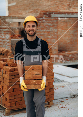 The bricks in hands, holding it. A builder is working at the construction site at daytime 139243883