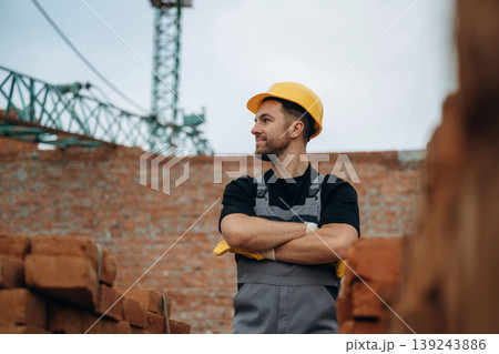 Front view, standing. A builder is working at the construction site at daytime Front view, standing. A builder is working at the construction site at daytime 139243886