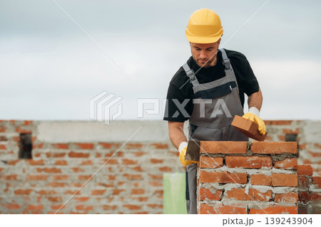 Placing the bricks, making a wall. A builder is working at the construction site at daytime Placing the bricks, making a wall. A builder is working at the construction site at daytime 139243904