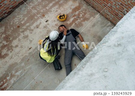 Top view. Man, construction worker fell from big height, lying down without consciousness, accident, woman is checking Top view. Man, construction worker fell from big height, lying down without consciousness, accident, woman is checking 139243929