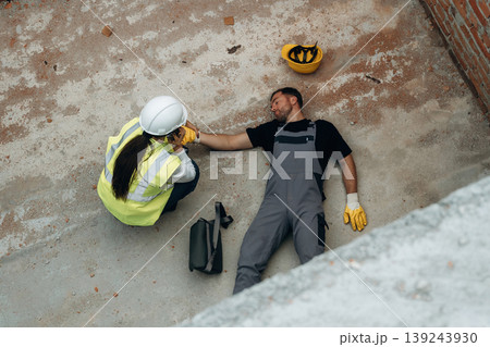 Top view. Man, construction worker fell from big height, lying down without consciousness, accident, woman is checking Top view. Man, construction worker fell from big height, lying down without consciousness, accident, woman is checking 139243930