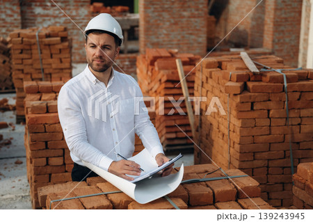 Writing information into notepad. A builder is working at the construction site at daytime Writing information into notepad. A builder is working at the construction site at daytime 139243945
