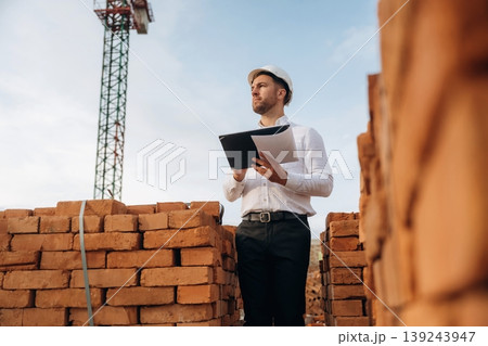 Writing information into notepad. A builder is working at the construction site at daytime Writing information into notepad. A builder is working at the construction site at daytime 139243947