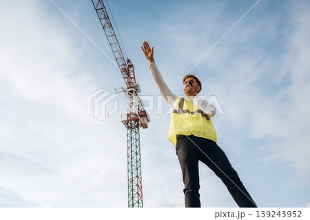 Radio communication, giving orders. Construction site worker is against building crane and sky background Radio communication, giving orders. Construction site worker is against building crane and sky background 139243952