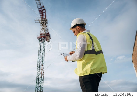 According to a plan. Construction site worker is against building crane and sky background According to a plan. Construction site worker is against building crane and sky background 139243966