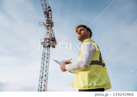 According to a plan. Construction site worker is against building crane and sky background According to a plan. Construction site worker is against building crane and sky background 139243968