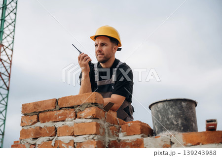Talking by walkie talkie. A builder is working at the construction site at daytime 139243988