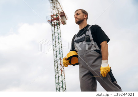 Break time, standing and posing. Construction site worker is against building crane and sky background Break time, standing and posing. Construction site worker is against building crane and sky background 139244021