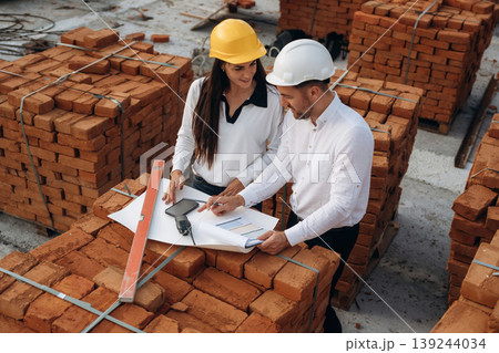 Discussing the plan, with documents. Female manager and male builder are on the construction site Discussing the plan, with documents. Female manager and male builder are on the construction site 139244034