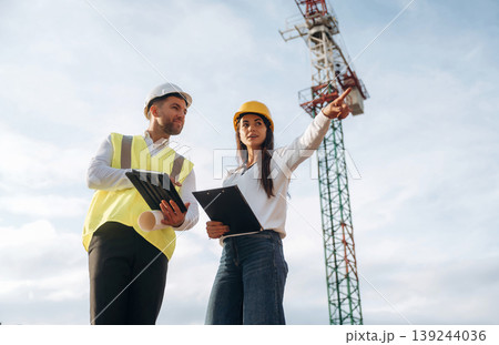 Man and woman, construction site workers are against crane, communication 139244036