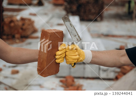 With brick. Side view of two hands of builders on construction site that are knocking the fists, conception of teamwork, unity With brick. Side view of two hands of builders on construction site that are knocking the fists, conception of teamwork, unity 139244041