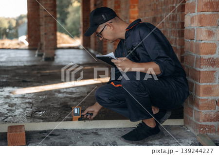 Checking if the level is right. Builder is working on construction site, unfinished building Checking if the level is right. Builder is working on construction site, unfinished building 139244227