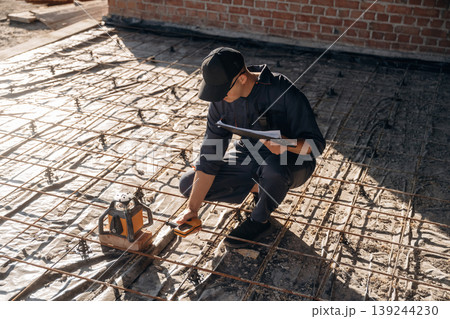 Checking if the level is right. Builder is working on construction site, unfinished building Checking if the level is right. Builder is working on construction site, unfinished building 139244230