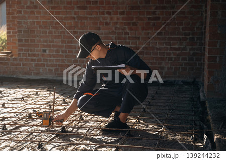 Sitting and using leveling tool. Builder is working on construction site, unfinished building 139244232