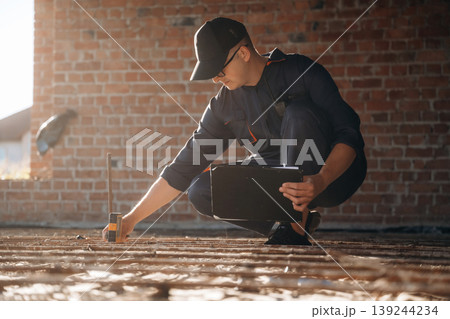 Sitting and using leveling tool. Builder is working on construction site, unfinished building Sitting and using leveling tool. Builder is working on construction site, unfinished building 139244234
