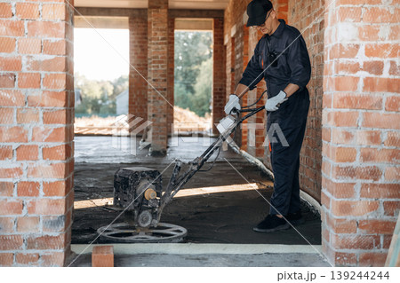 Process of leveling the concrete on the floor. Builder is working on construction site, unfinished building Process of leveling the concrete on the floor. Builder is working on construction site, unfinished building 139244244