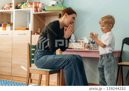Woman is sitting and checking the boy. Preschool child with teacher during developmental activities in a playroom Woman is sitting and checking the boy. Preschool child with teacher during developmental activities in a playroom 139244282